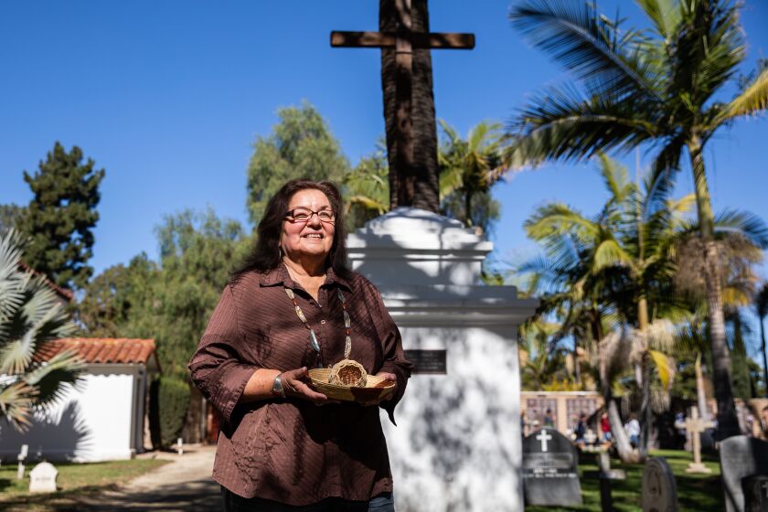 Oceanside, CA - November 10: Diania Caudell poses for a portrait holding a Luseno and Cherokee style baskets she weaved in front of the Indian Memorial at Mission San Luis Rey in Oceanside, CA on Thursday, Nov. 10, 2022. Caudell is a member of the San Luis Rey Band of Mission Indians and is on the board of the California Indian Basketweavers Association. (Adriana Heldiz / The San Diego Union-Tribune)