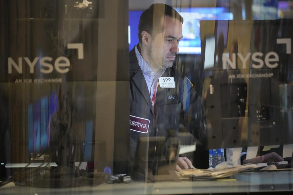 A trader looks at a screen behind a glass window with the New York Stock Exchange logo on it.