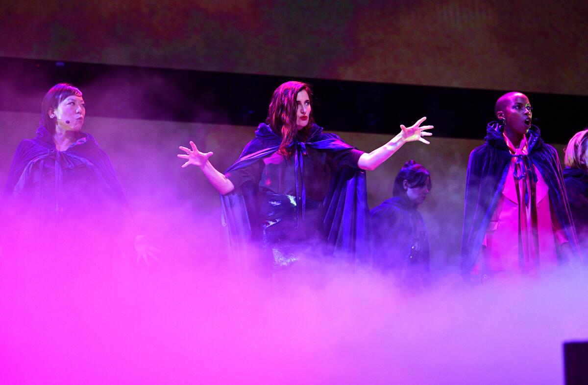 Four people dressed in capes on a foggy stage.