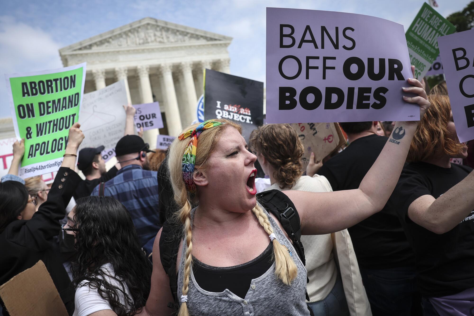 A young woman holds a sign reading, "Bans off our bodies."