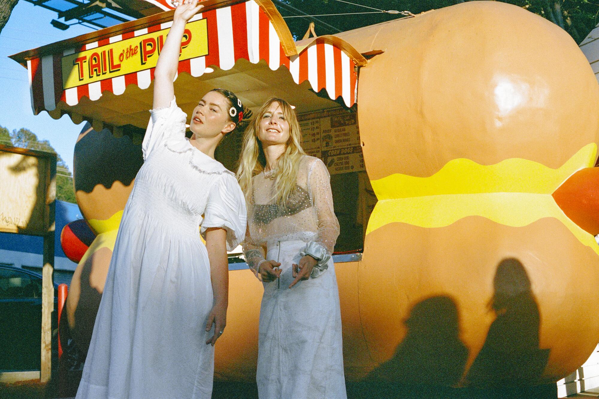 Two female musicians pose in front of a hot dog stand