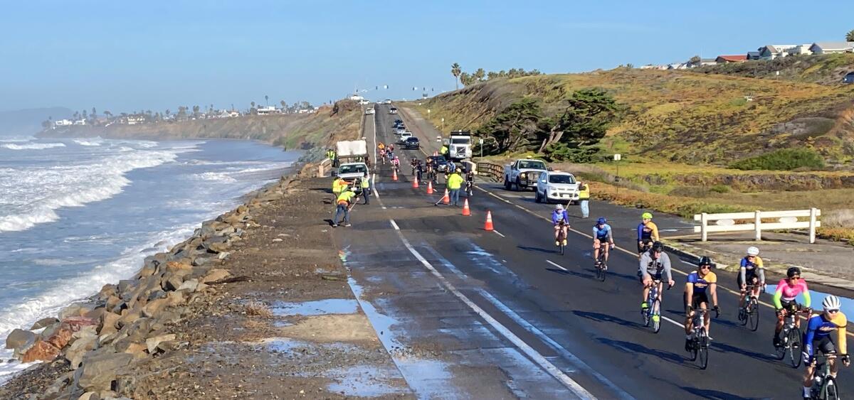 Cyclists pass a road-cleaning crew on Carlsbad Boulevard after a high tide in January.