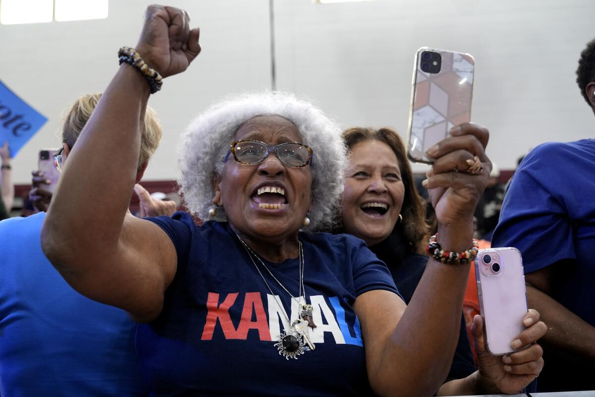 A woman in a red, white and blue "Kamala" shirt raises her arms and cheers.