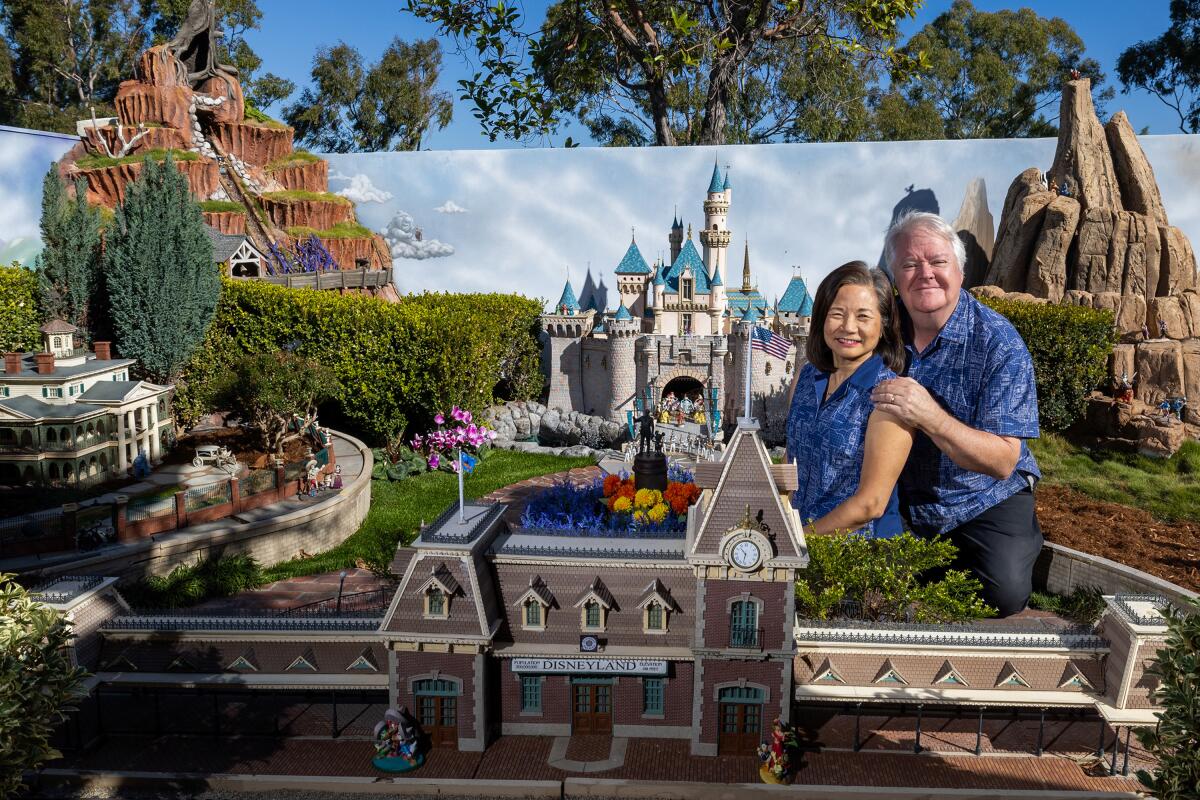 A couple pose in front of the miniature Disneyland in their yard.