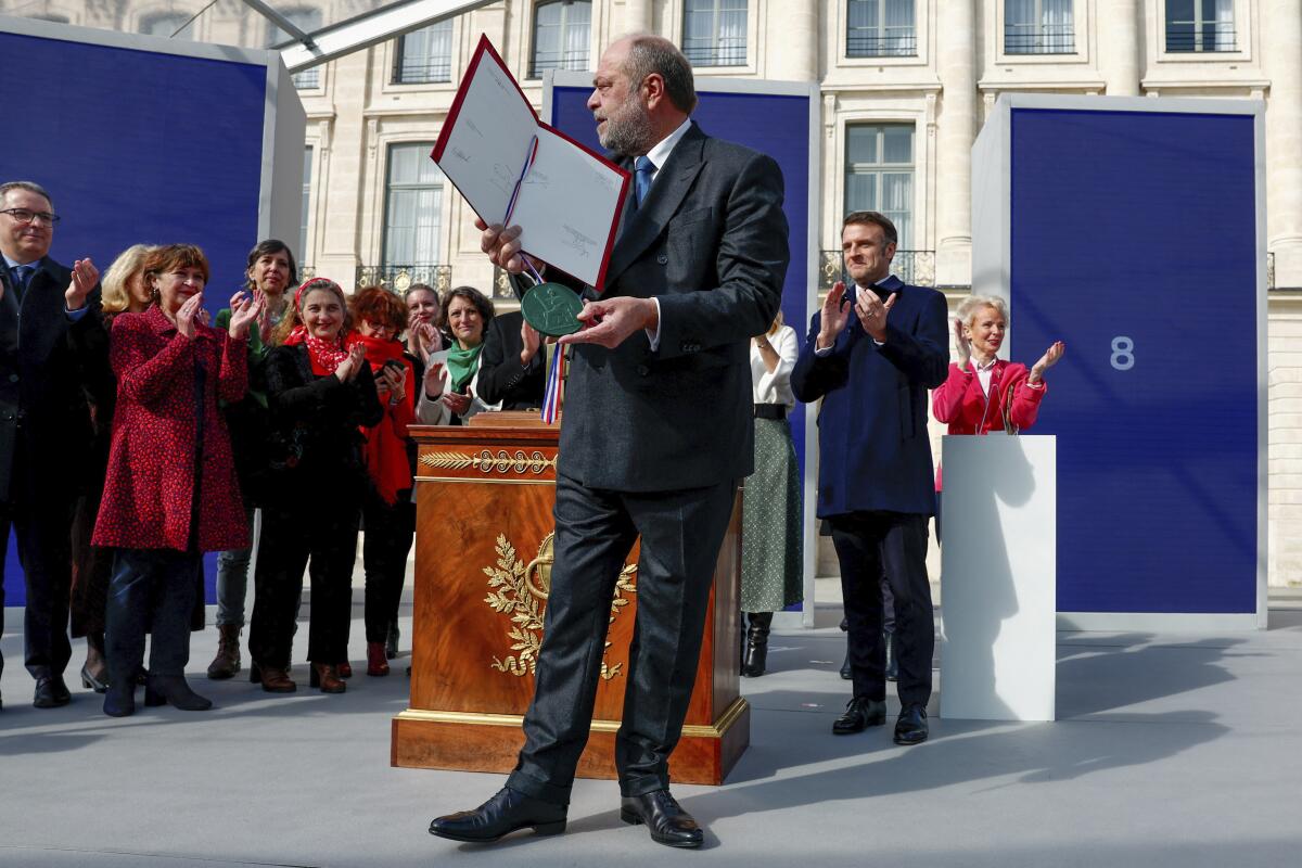 A man holds up a folder with papers as people around him clap.