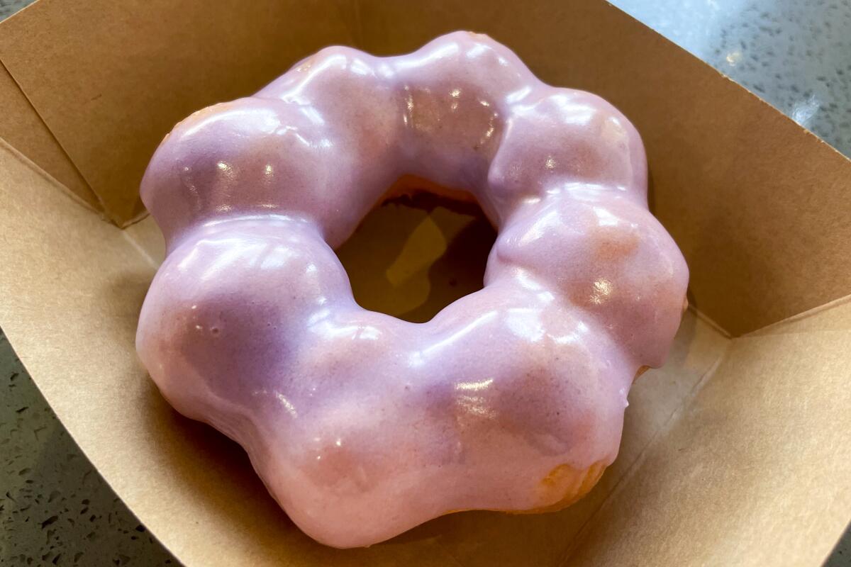 A pink frosted doughnut in a cardboard tray