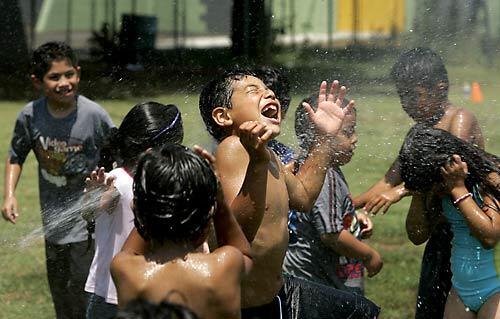 Victor Osorto, center, enjoys the spray from a sprinkler along with other children attending a Para Los Ninos summer camp in Pecan Playground in the Boyle Heights. Forecasters are predicting continued sizzling temperatures for the Southland this weekend.