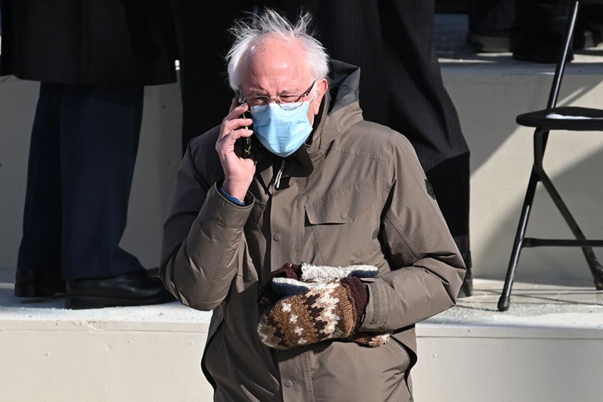 A masked Sen. Bernie Sanders, wearing one mitten and holding another one, talks on the phone.