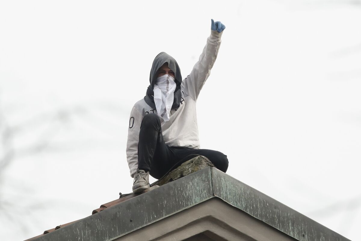 A man gestures from the roof of San Vittore prison in Milan, Italy, during an inmate protest Monday. 