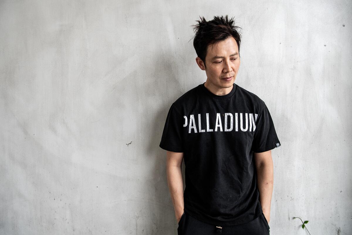Chef Kenji Tang, wearing black pants and black T-shirt with the word Palladium in white, leans against a wall.