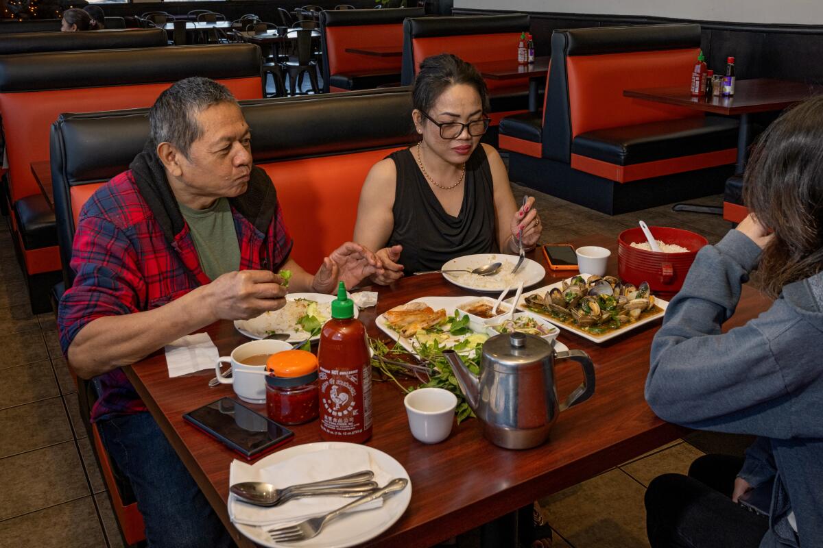 A man and a woman sit at a red banquette in a Cambodian restaurant with several plates of food on their table