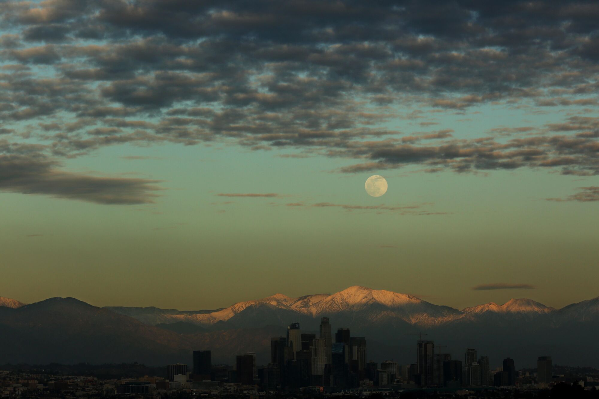 The moon rises above the snowcapped San Gabriel mountains and the Los Angeles skyline