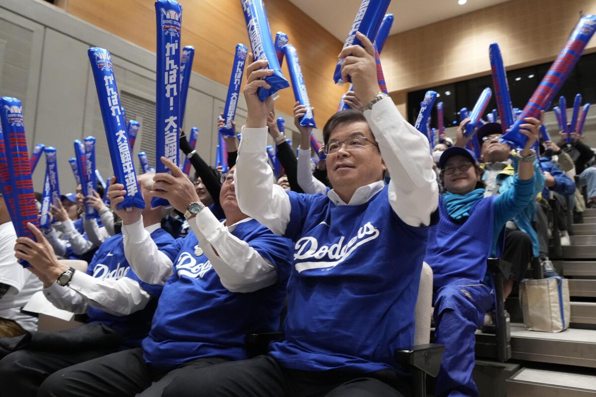 People in Dodger jerseys hold blue lightning bolts in an auditorium.