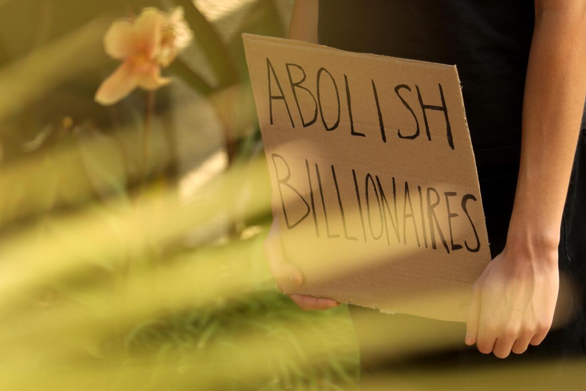 A person holds a cardboard sign with the words "Abolish billionaires."