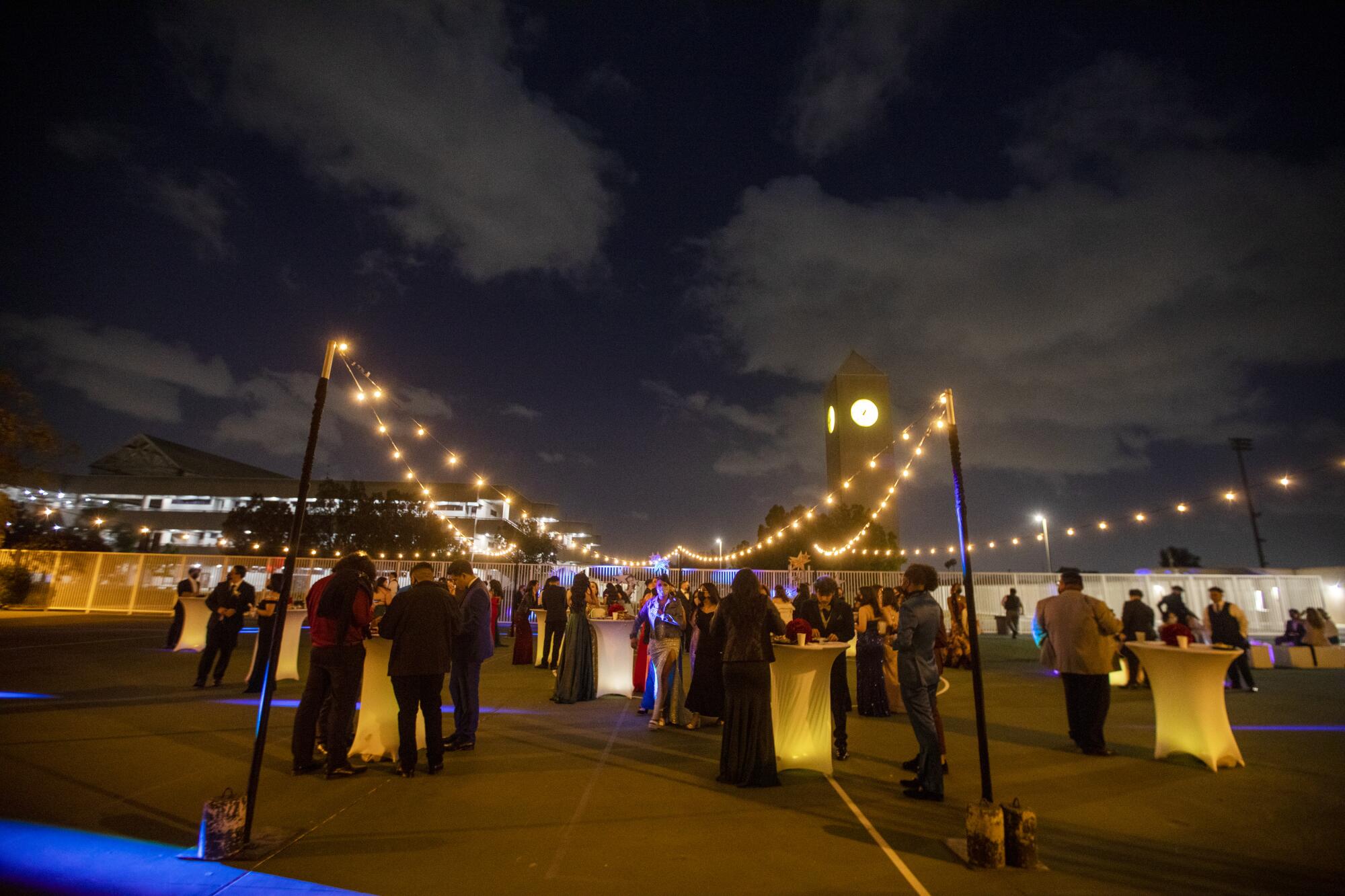 Students stand under string lights in prom attire