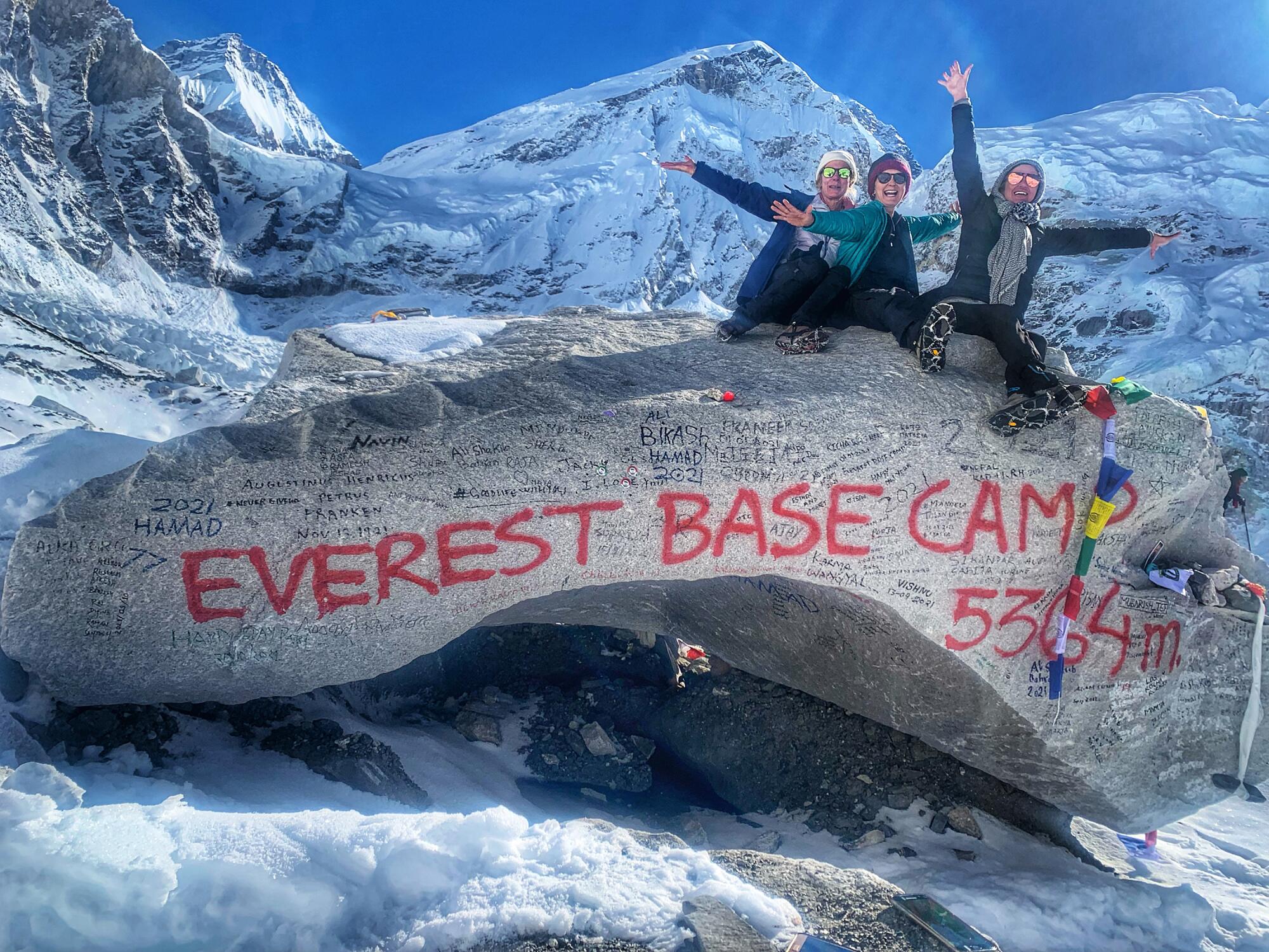 Three women celebrate atop a rock marking Everest Base Camp in Nepal, elevation 5,364 meters, or approximately 17,598 feet.
