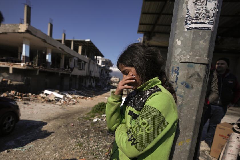A girl stands next to destroyed buildings in Antakya, southern Turkey, Wednesday, Feb. 8, 2023. Thinly stretched rescue teams worked through the night into Wednesday, pulling more bodies from the rubble of thousands of buildings downed in Turkey and Syria by a catastrophic earthquake. (AP Photo/Khalil Hamra)