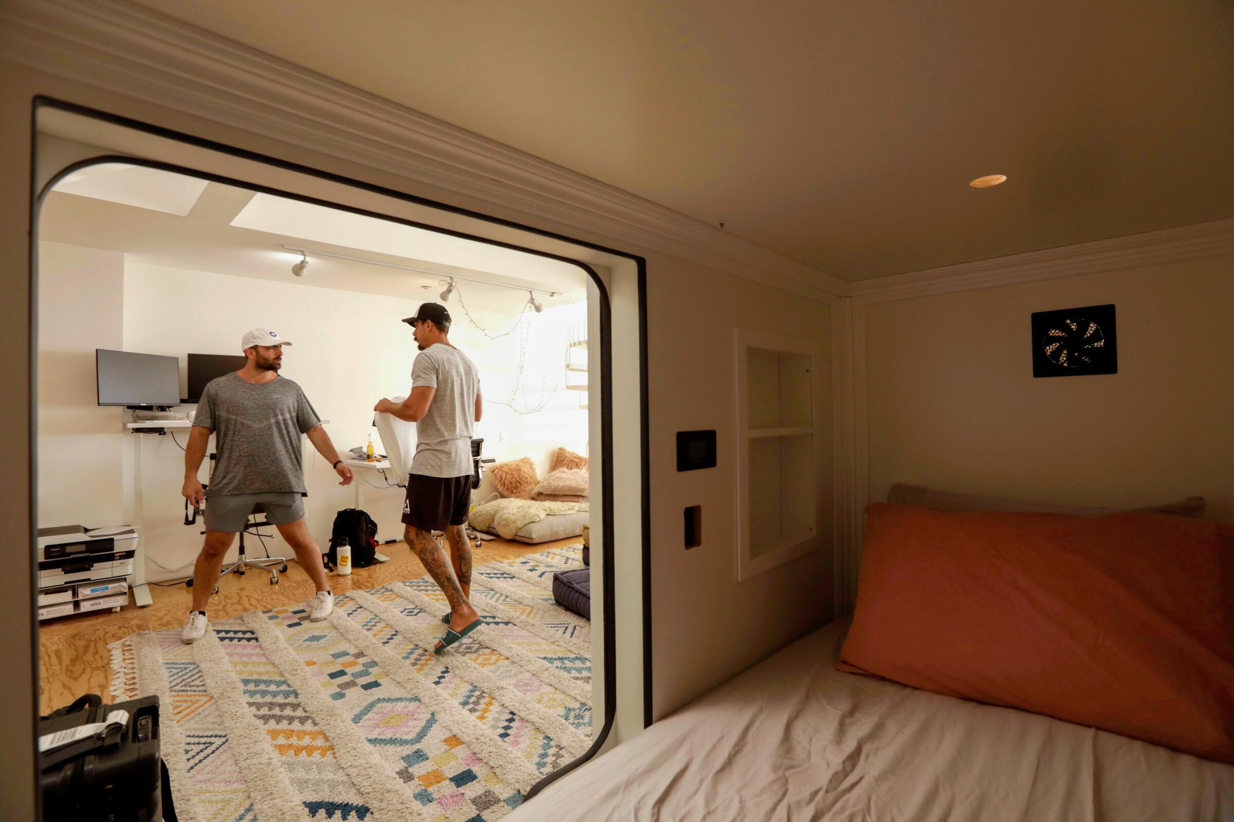 Two people, seen through the opening to a sleeping pod at a hotel.