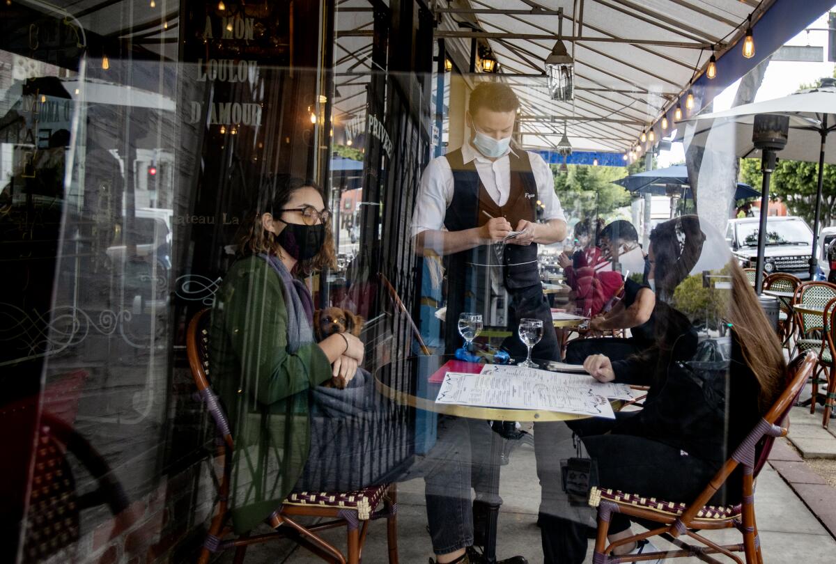 A waiter serves customers behind a plexiglass partition at a Figaro Bistrot in Los Feliz.