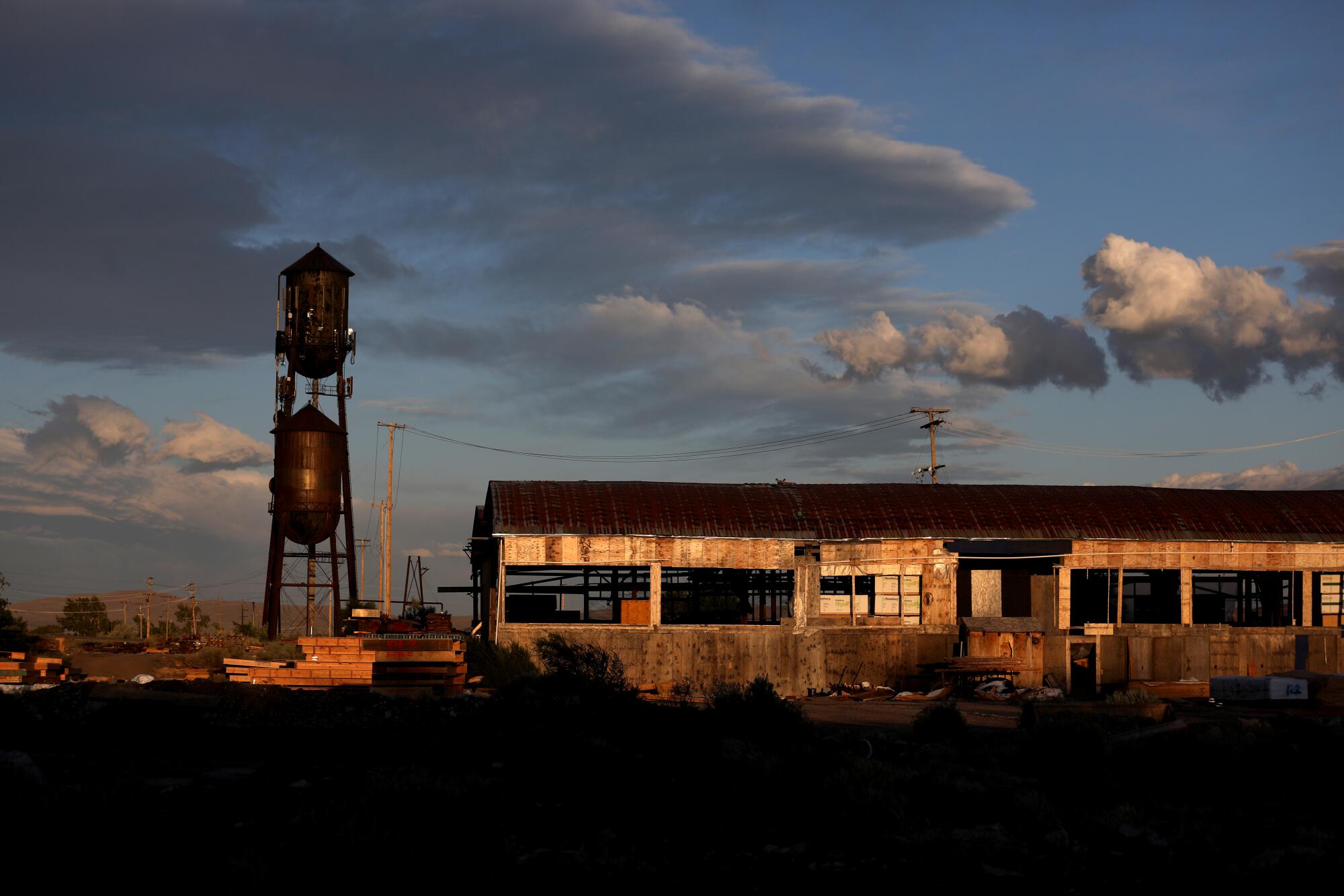 A rusting, empty building in a rural setting is seen at sunset.