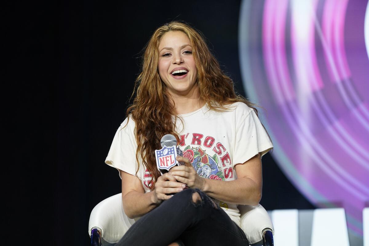 A smiling woman holding a microphone sits on a stage