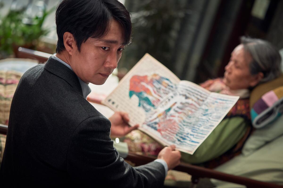 A man holds a booklet but looks away, behind him