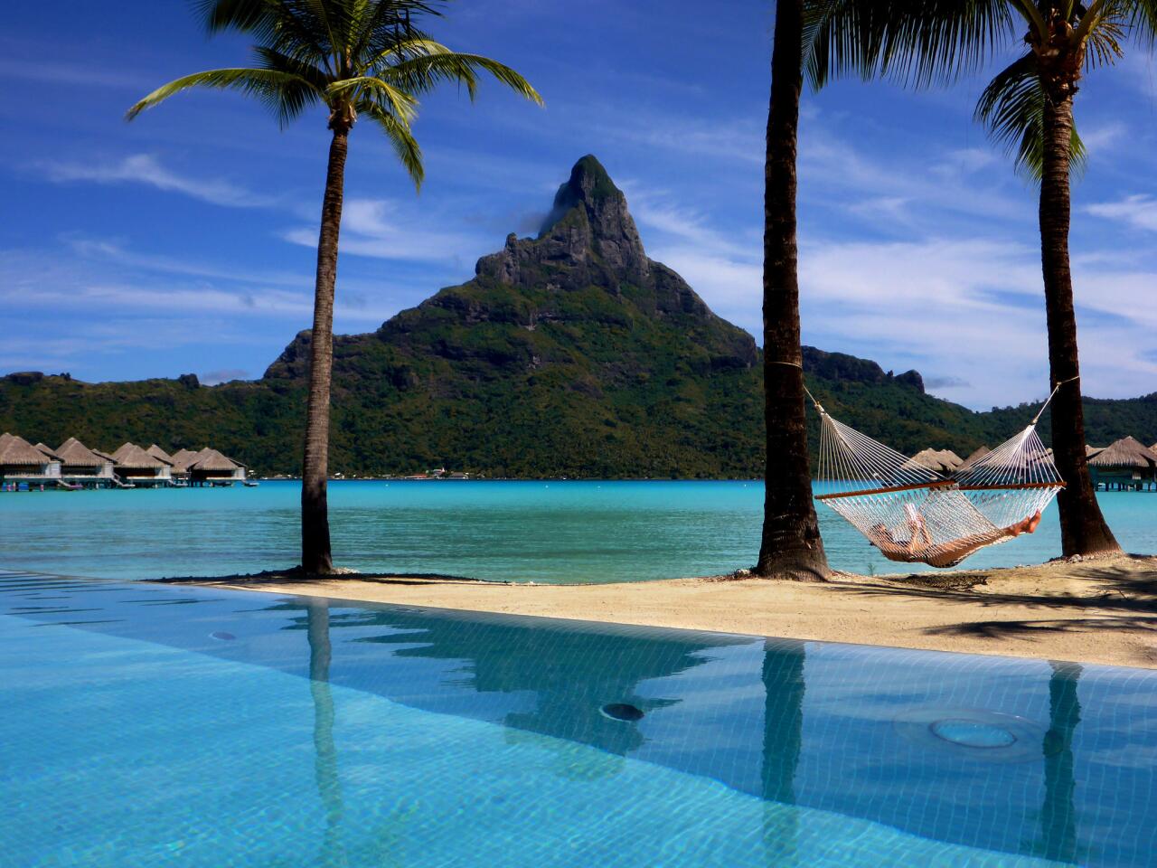 A guest reads a book on the beach at the InterContinental Bora Bora Resort and Thalasso Spa, commonly called the Thalasso, in Bora-Bora. Mt. Otemanu looms in the background.