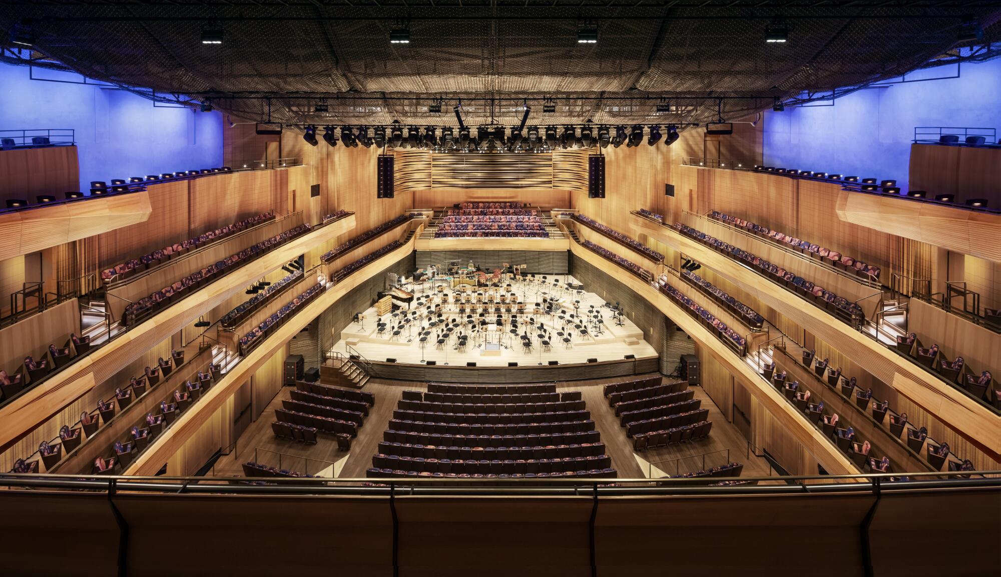 A concert hall clad in blond wood with a bright maple stage is seen from an upper tier.