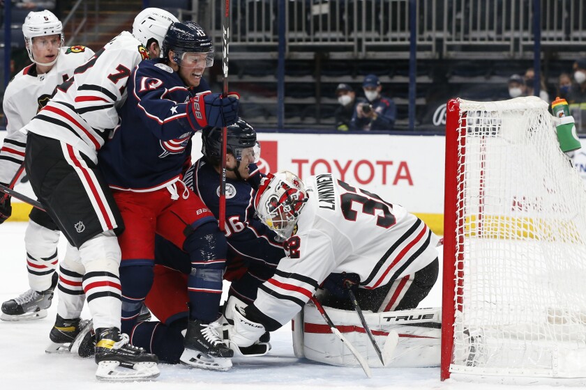 Chicago Blackhawks' Kevin Lankinen, right, covers the puck as teammate Kirby Dach, left, and Columbus Blue Jackets' Cam Atkinson, left center, and Jack Roslovic fight for position during the second period of an NHL hockey game Saturday, April 10, 2021, in Columbus, Ohio. (AP Photo/Jay LaPrete)