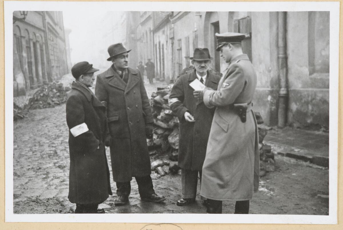 A German policeman checks the identification papers of Jewish people in the Krakow ghetto in Poland, circa 1941.