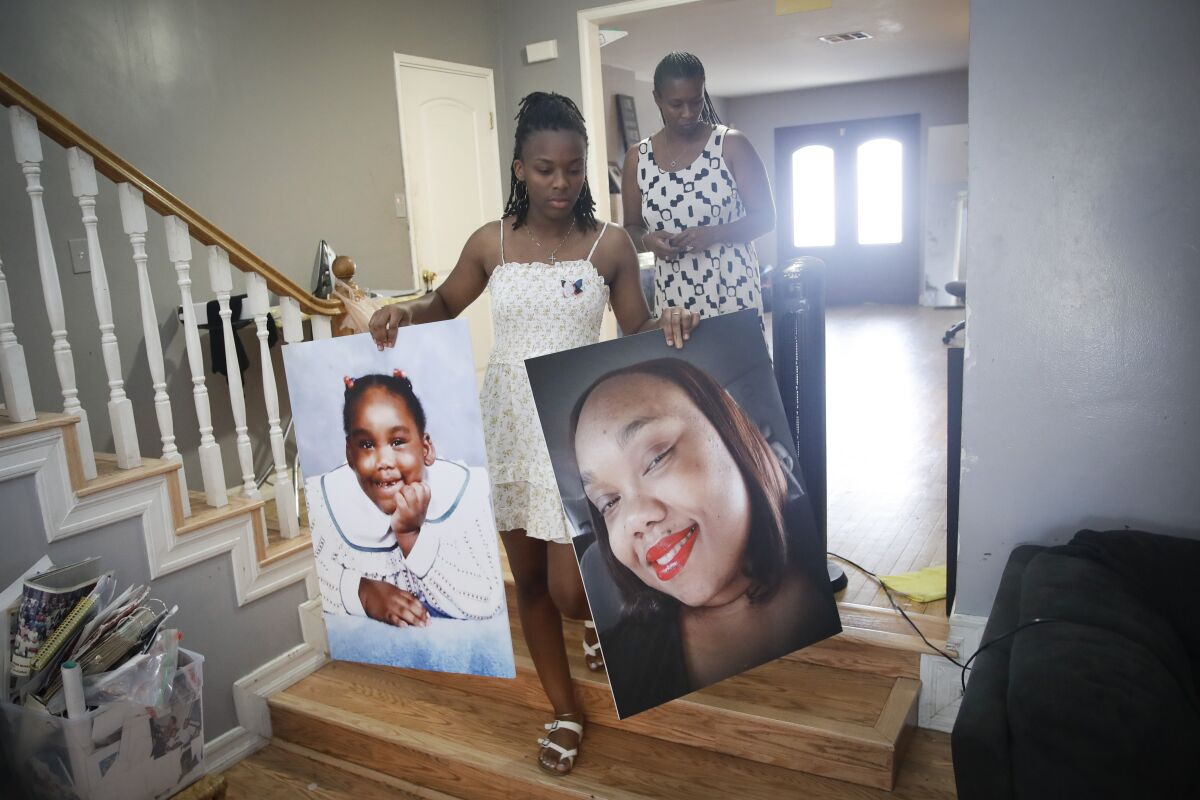 Eryanna Banks, left, carries photos of her Aunt Lydia Nunez, who died from COVID-19, in front of her mother Erika at the end of the day following a memorial service and burial for Nunez Tuesday, July 21, 2020, in Los Angeles. (AP Photo/Marcio Jose Sanchez)