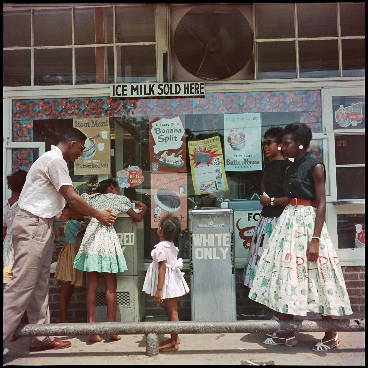 A Black man helps a little girl drink from a "Colored" drinking fountain in 1956.