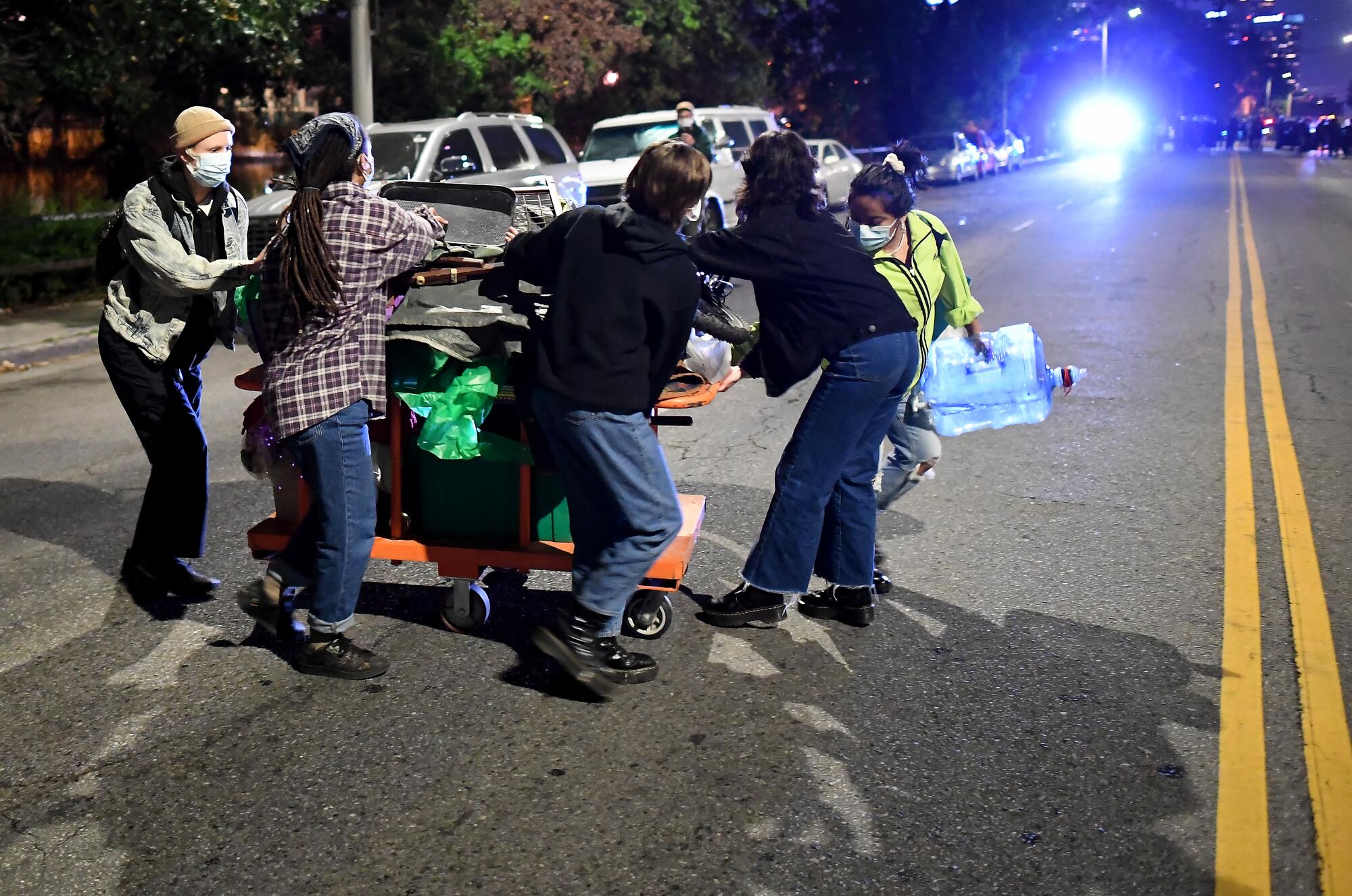 People move a cart of belongings across a road.