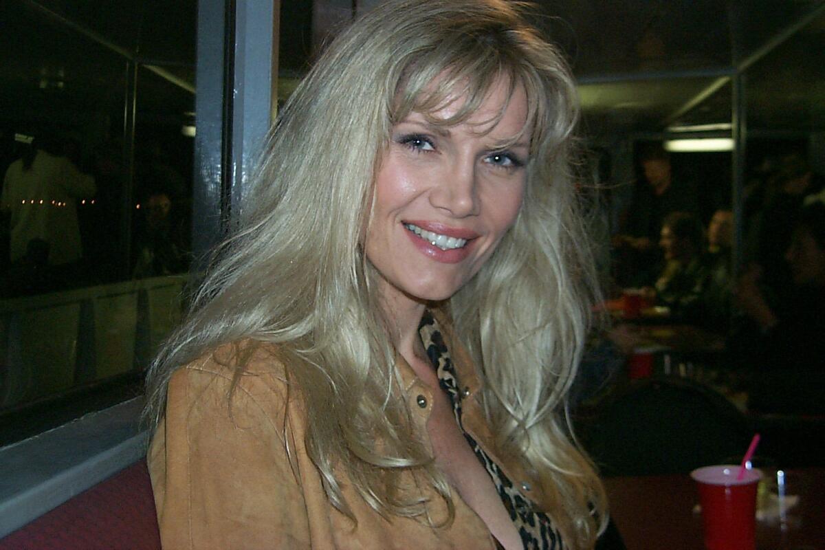 A blond woman seated in a restaurant booth smiles at the camera.