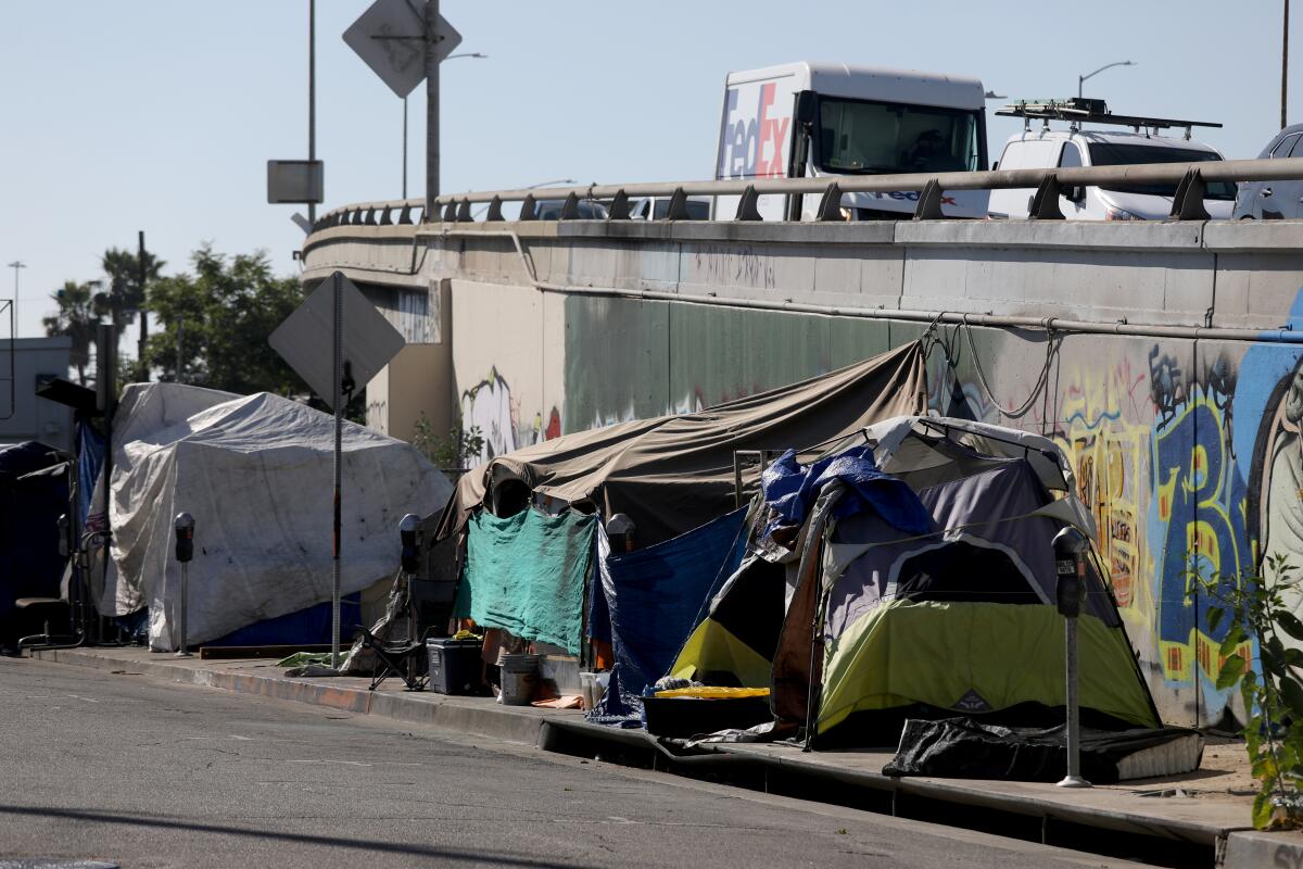 A homeless encampment on the sidewalk along a freeway