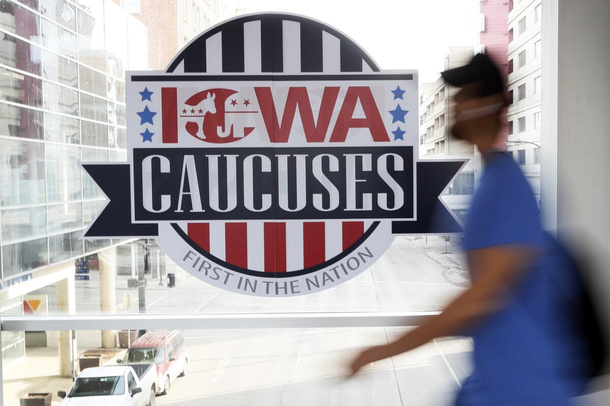 The blur of a person approaching a sign reading "Iowa caucuses/First in the nation," posted on a walkway above a city street