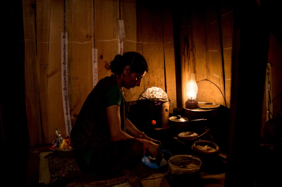 Anita Chauhan works in the kitchen illuminated by a kerosene lamp as their residence in Barnali Village awaits electrification.