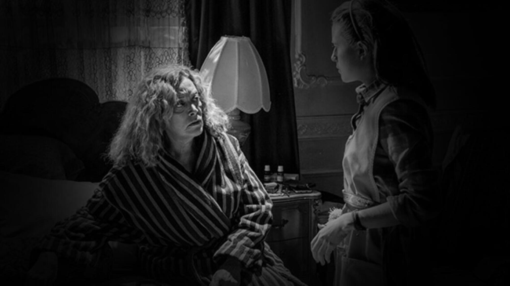 A black-and-white film still of a disheveled woman speaking to another woman in shadow.