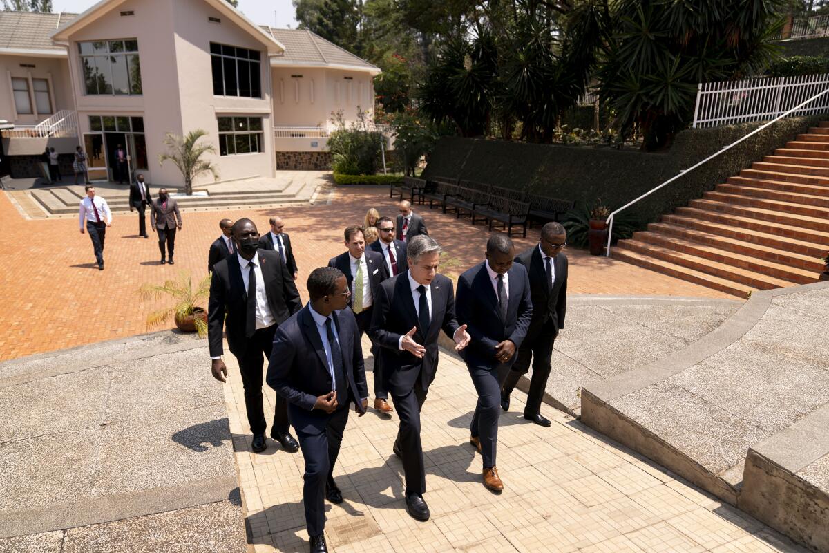 Secretary of State Antony J. Blinken and a group of men, all in dark suits and ties, walk on a ramp 