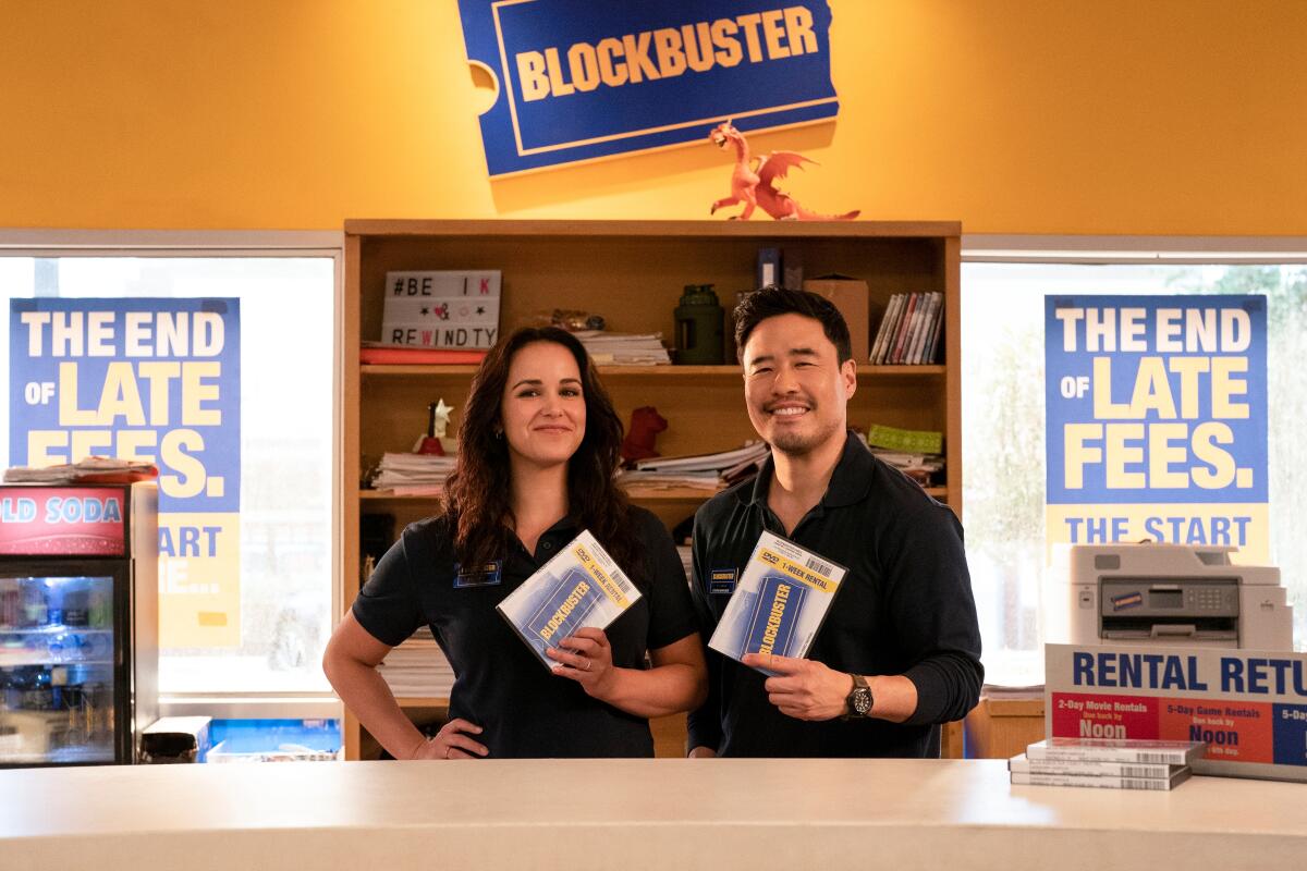 Two Blockbuster employees posing with DVDs behind the counter.