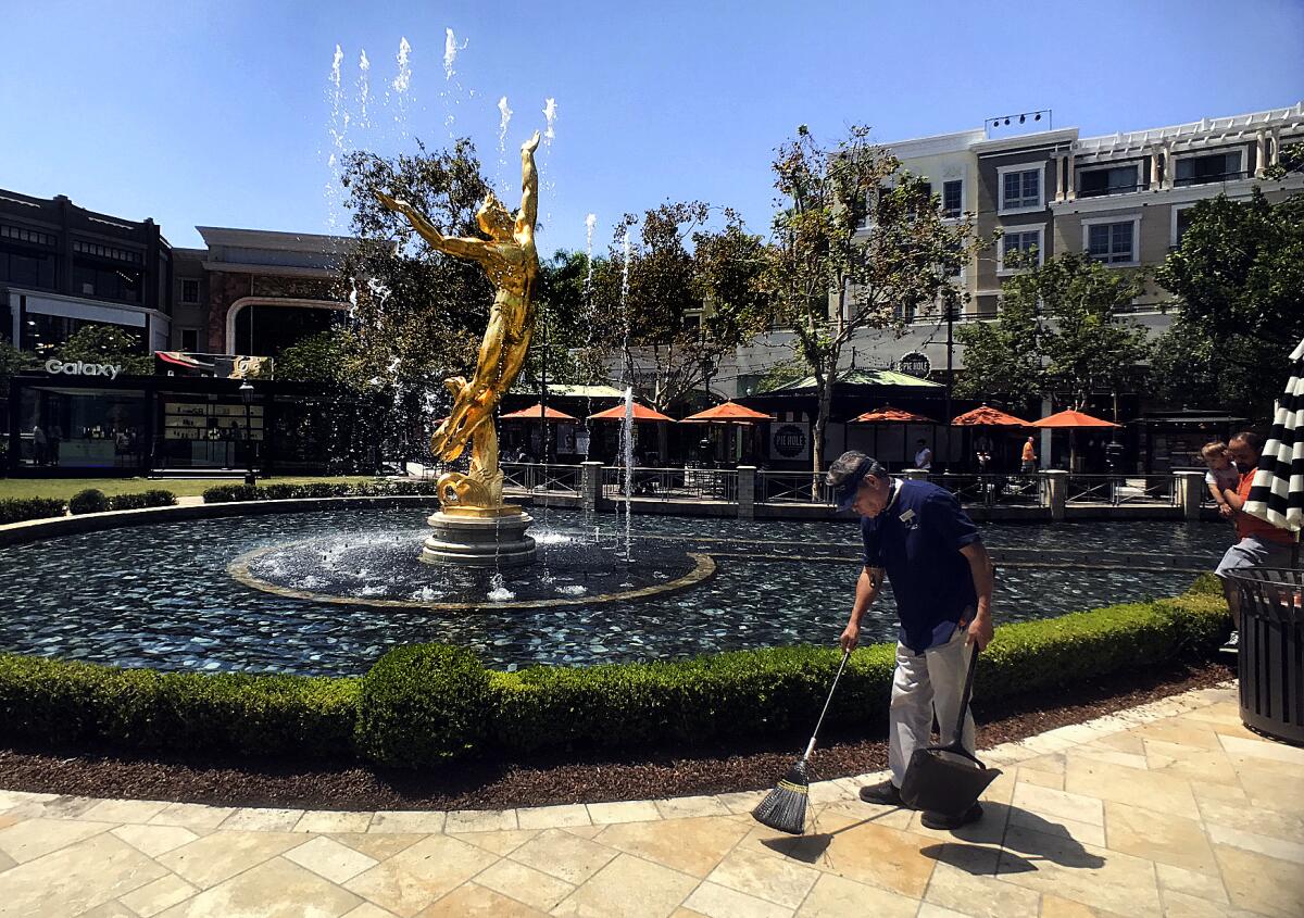 A custodian is seen sweeping before a large fountain 
