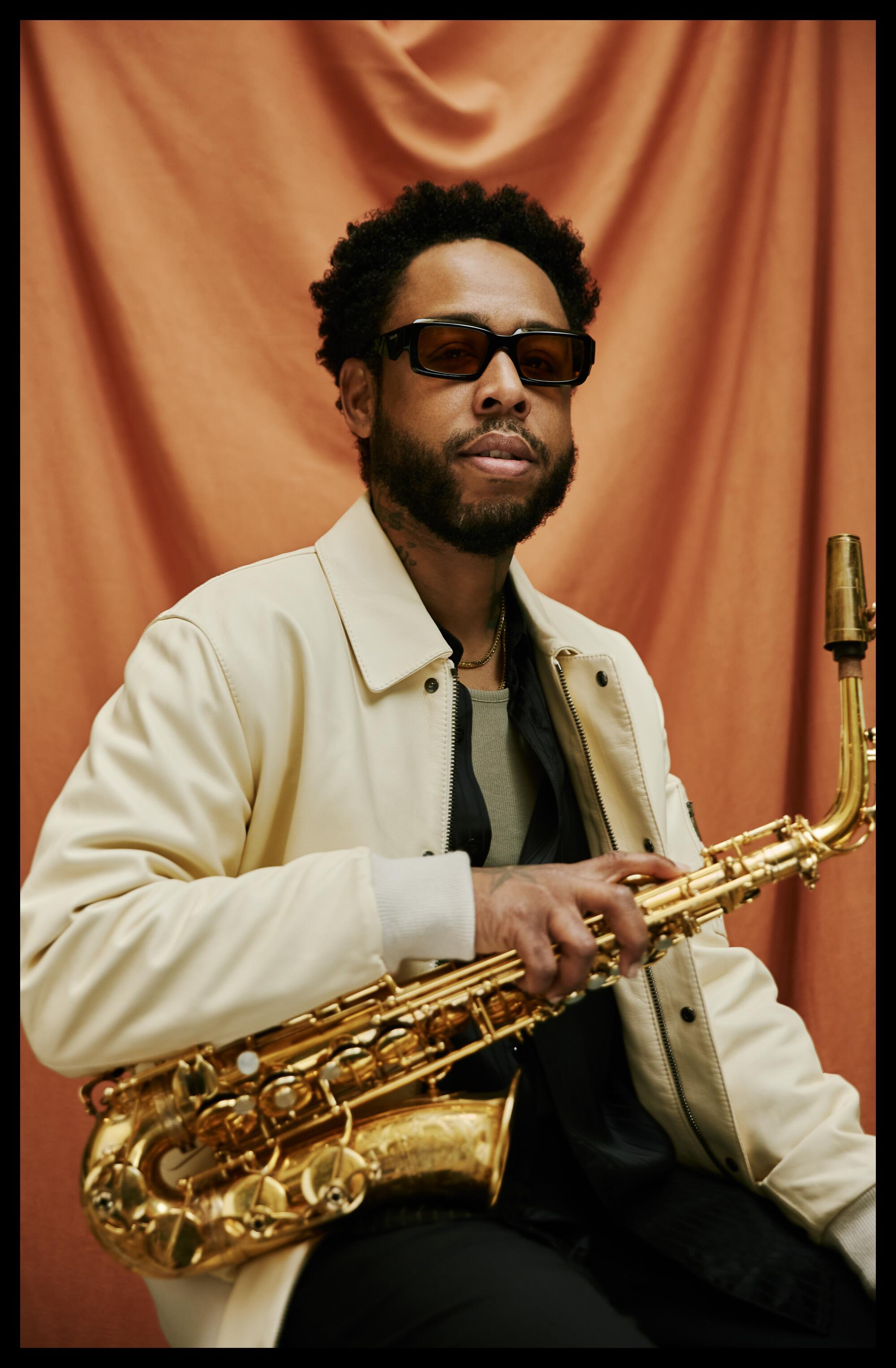 The musician Terrace Martin holds his saxophone, an orange cloth backdrop behind him.