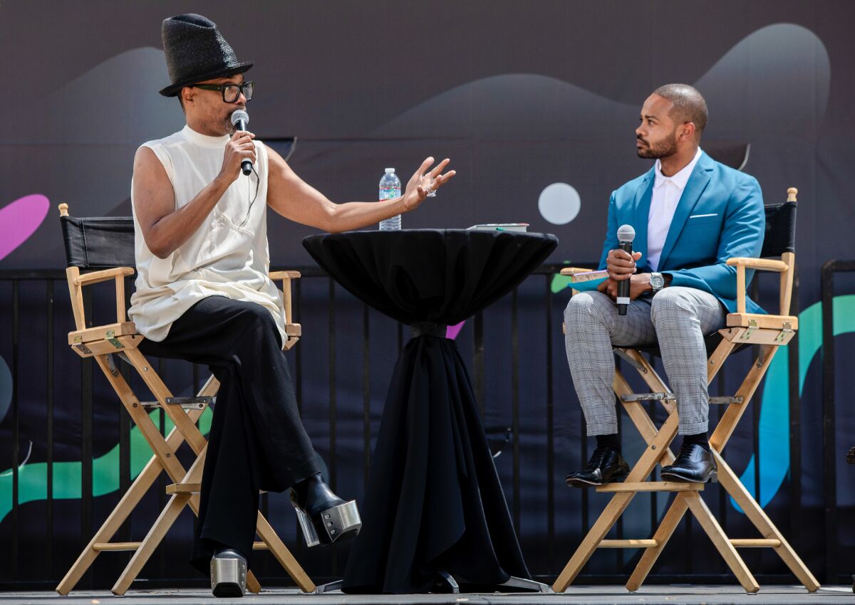 Billy Porter gestures with one hand and holds a microphone in the other while onstage next to Justin Ray