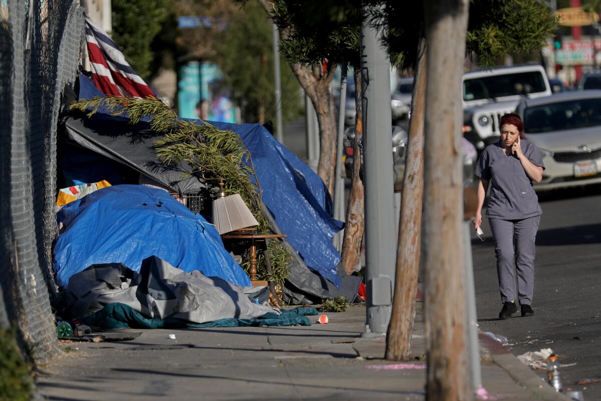 A woman walks in the street because a homeless encampment is blocking the sidewalk.
 
