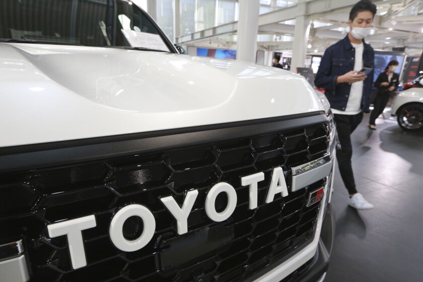FILE - A man walks by the logo on a Toyota car at a showroom in Tokyo on Oct. 18, 2021. The shortage of parts caused by the coronavirus pandemic is further denting production at Toyota, Japan’s top automaker. (AP Photo/Koji Sasahara, File)
