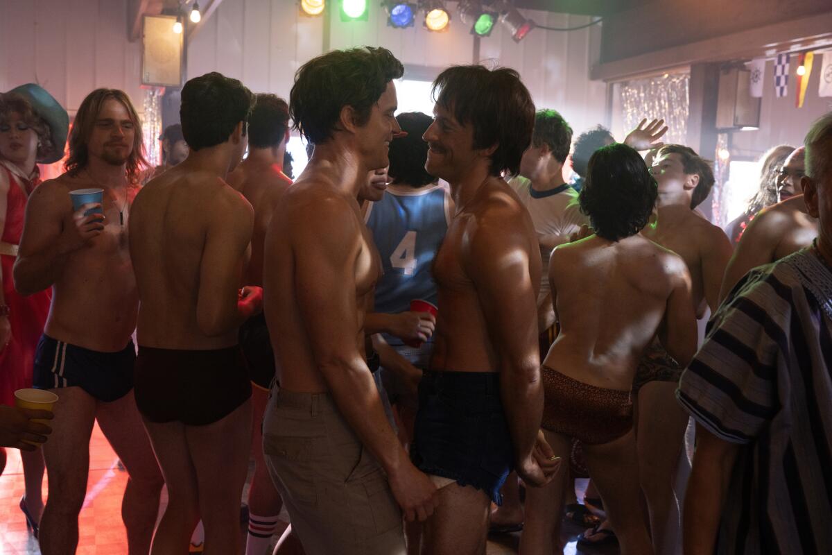 Surrounded by shirtless men, Hawk and Tim dance together.