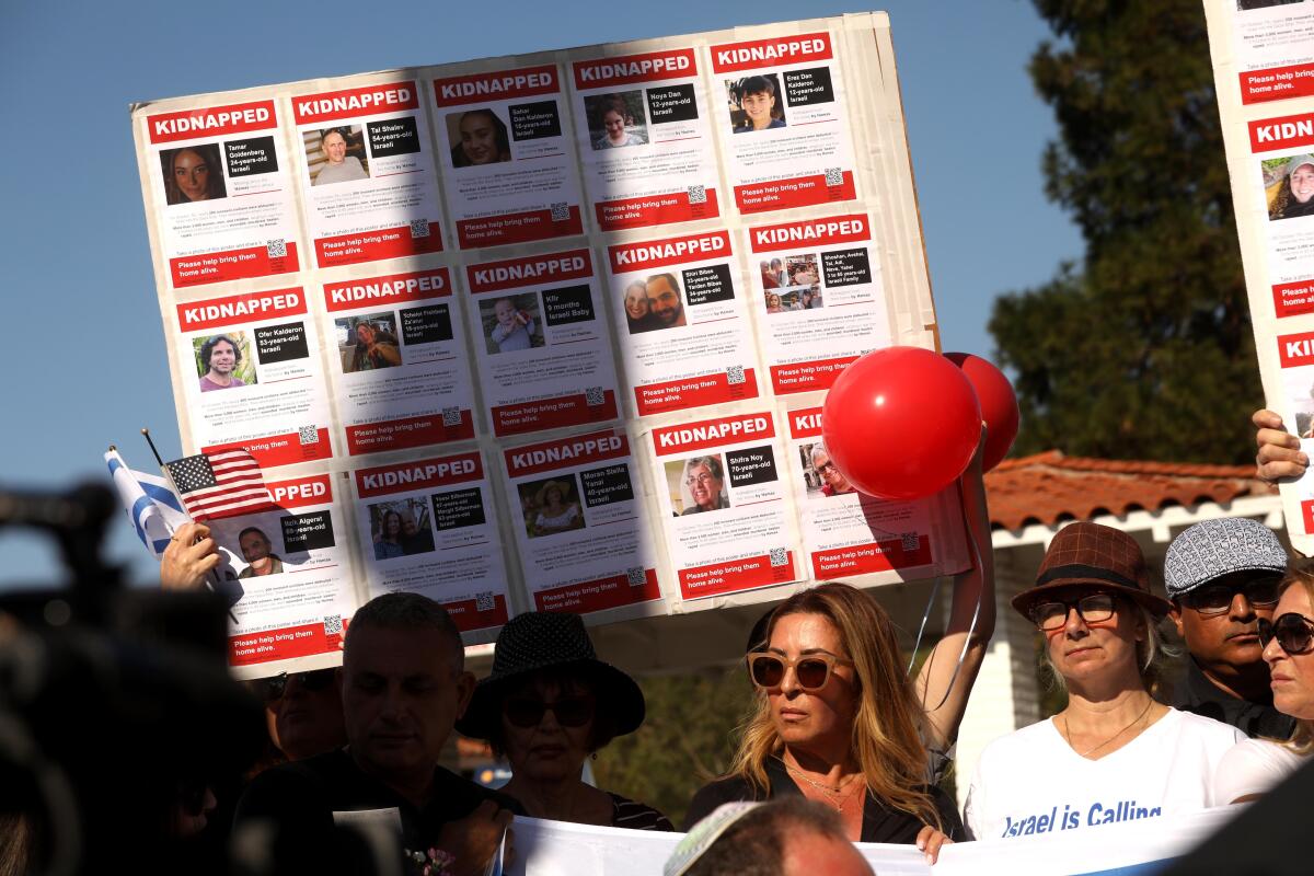 People hold up balloons and signs with pages of photos and writing.