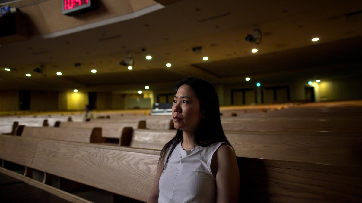 Priscylla Lee in a white sleeveless top, looking ahead from her seat in otherwise empty church pews