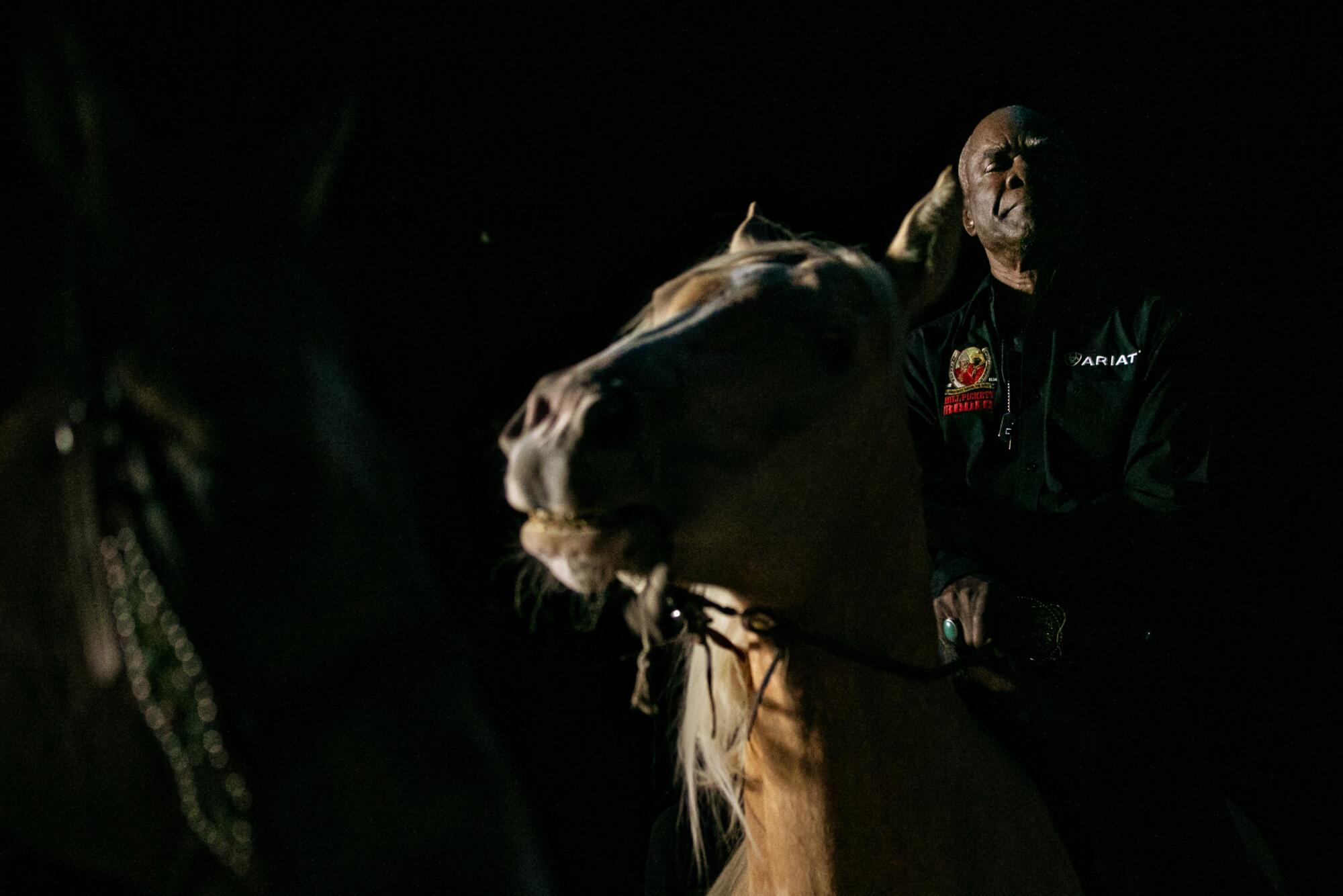 A man sits on a horse in a mostly darkened arena