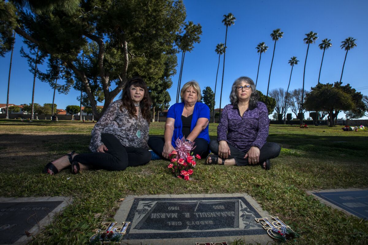 Three women with flowers sitting near a headstone